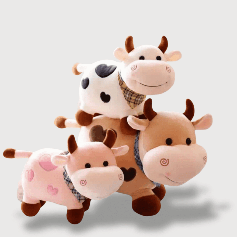 Doudou Vache Souriante 25 cm : Trois adorables doudous vaches au sourire tendre : l’une blanche à taches noires, une autre rose avec des cœurs, et la dernière beige avec un joli foulard.