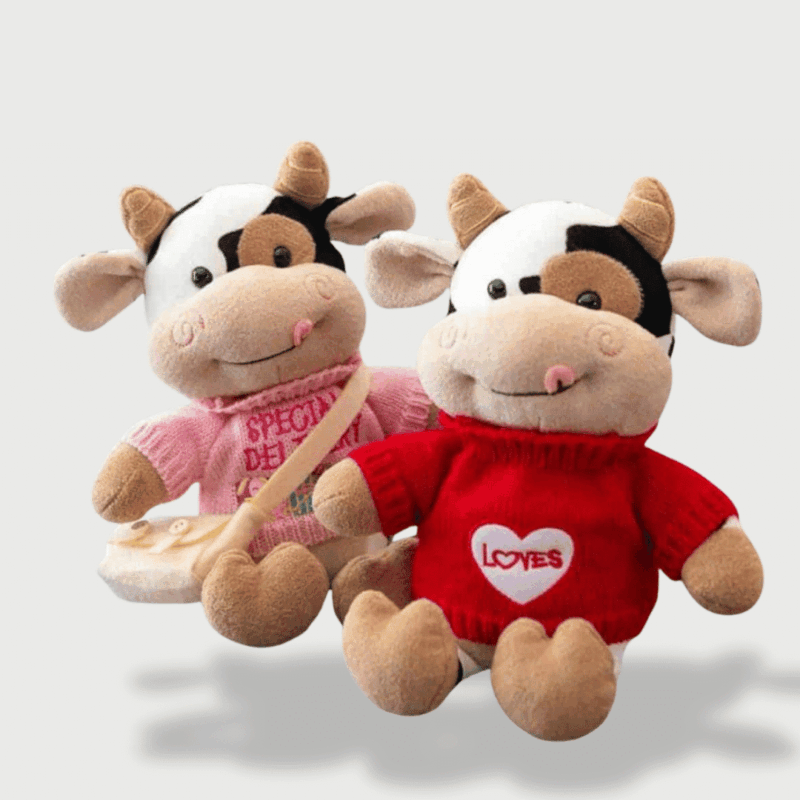Doudou Vache Fashion 30 cm : Deux doudous vaches assis, l’un avec un pull rouge "Love" et l’autre avec un pull rose et un sac à main.