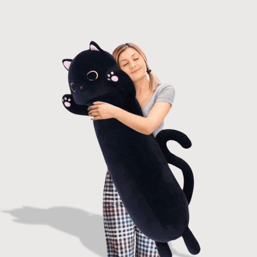 Doudou Chat Noir Géant : Une femme blonde en pyjama est en train de faire un câlin à un doudou chat noir XXL avec des yeux dorés, idéal pour les câlins.