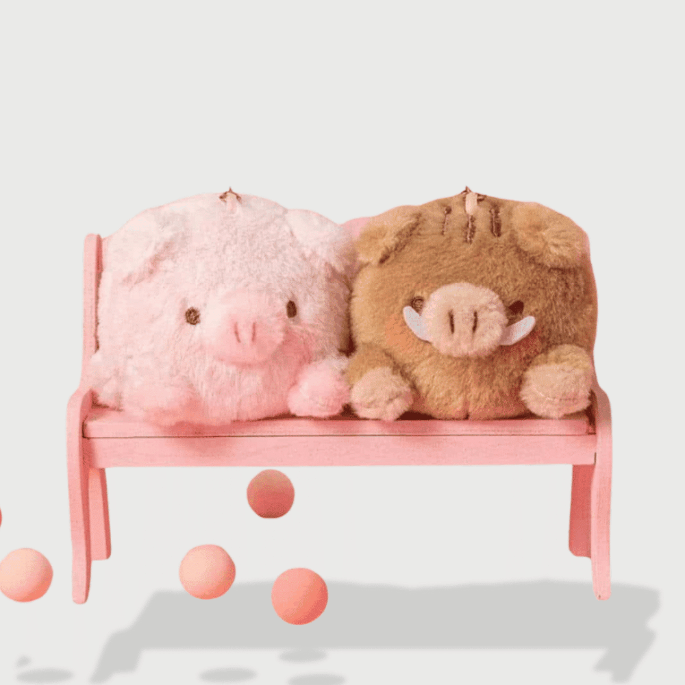 Doudou Cochon Kawaii Mini : Deux doudous, un cochon rose et marron, assis sur un banc rose entouré de balles.