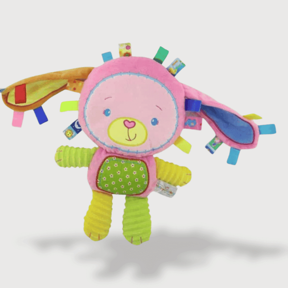 Doudou Musical Ours Déguisé en Lapin 33 cm avec un corps coloré, de longues oreilles et des étiquettes sensorielles.