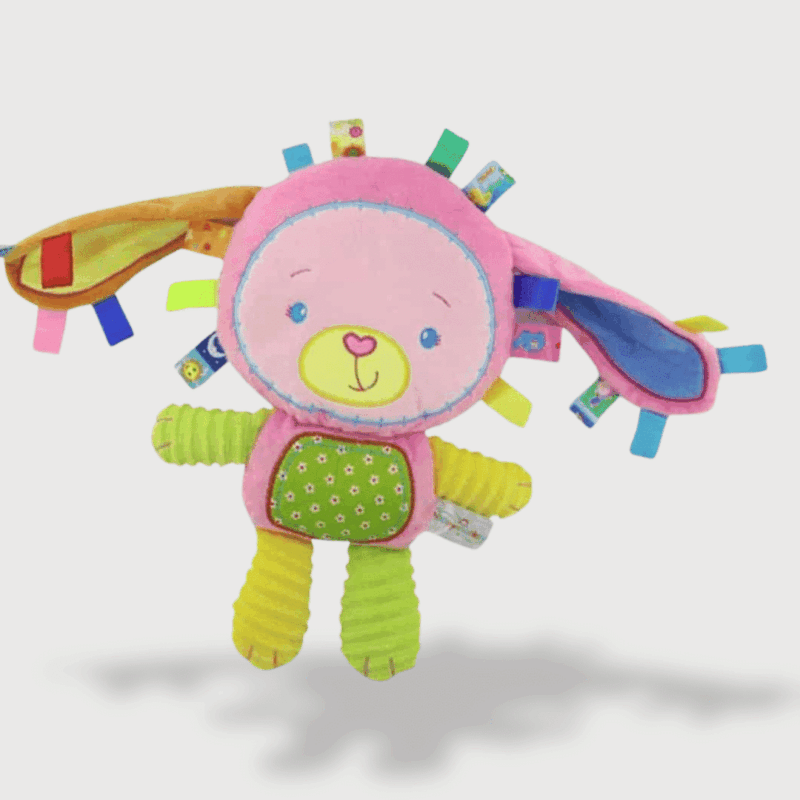 Doudou Musical Ours Déguisé en Lapin 33 cm avec un corps coloré, de longues oreilles et des étiquettes sensorielles.