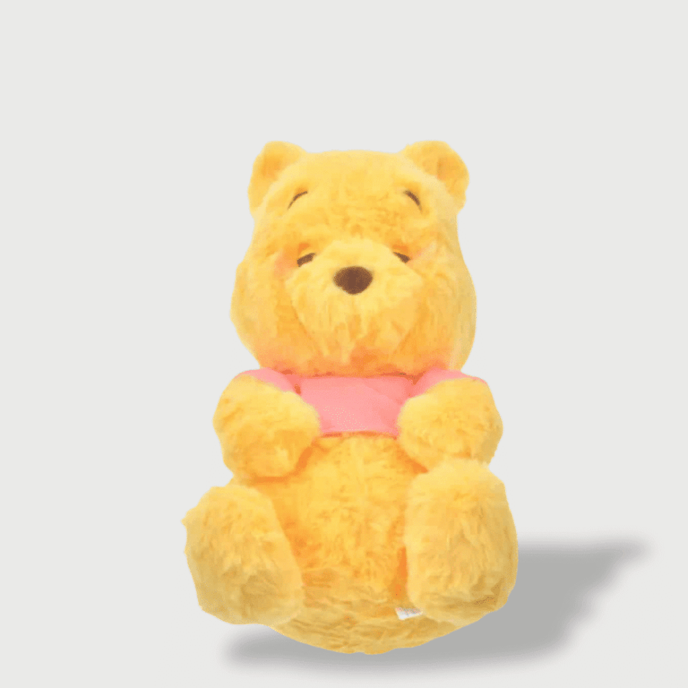 Doudou Winnie Dormant 32 cm, jaune en position assise, les yeux fermés, portant un t-shirt rose.