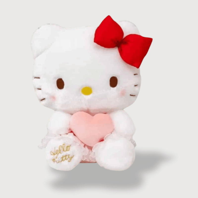 Doudou Kittie Très Mignon : Un doudou Hello Kitty blanc avec un nœud rouge et un coussin rose en forme de cœur entre les pattes.
