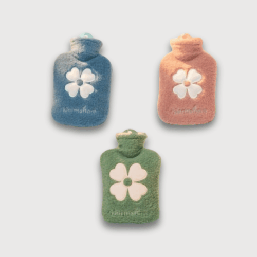 Doudou Bouillotte Portable pour Fille : Trois bouillottes en tissu pelucheux avec un motif de fleur blanche disponibles en plusieurs couleurs : vert, rose et bleu.