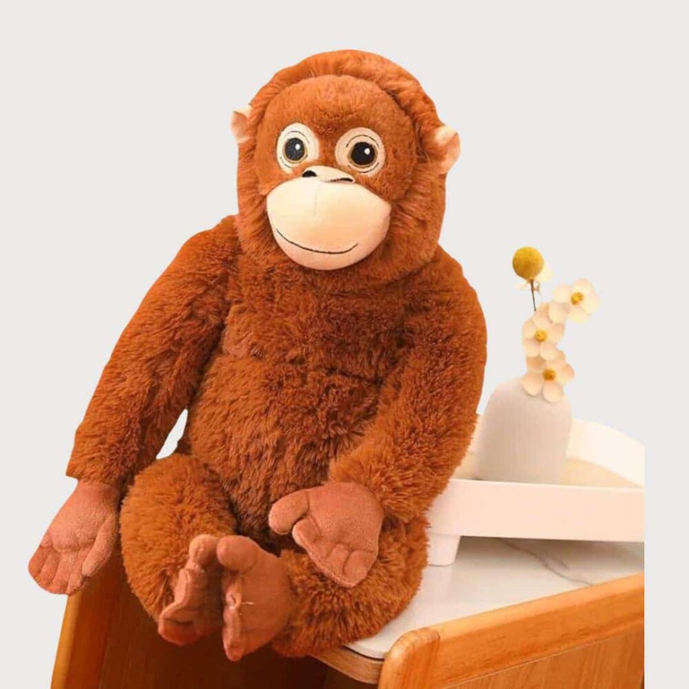 Doudou Singe Orang-Outan 66 cm représentant un grand orang-outan marron assis sur un meuble.